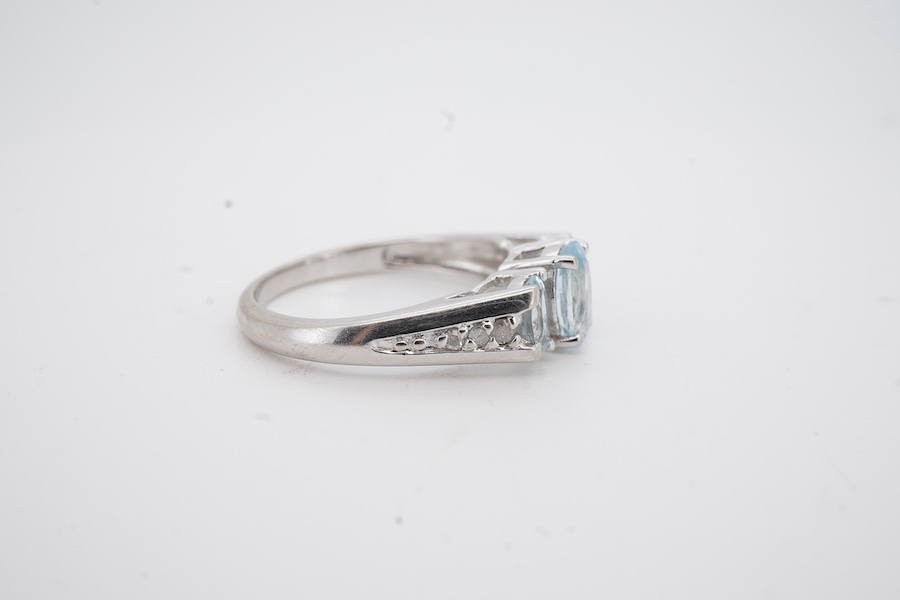 A modern 10k white metal and three stone oval cut aquamarine ring, with six stone diamond chip set shoulders, size N, gross weight 2.7 grams.
